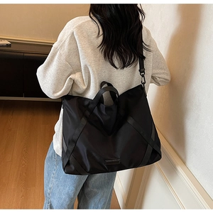 Nahaufnahme der schwarzen Nylon-Reisetasche mit breiten Schultergurten und Metall-Namensschild
