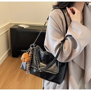 Detail of black leather underarm bag with gold chain strap and brown teddy bear charm