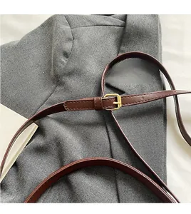 Close-up of adjustable brown leather shoulder strap with gold buckle on gray blazer