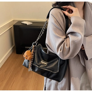 Detailed view of black pleated leather shoulder bag with chain strap and teddy bear charm
