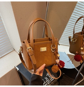 Close-up of brown suede bucket bag featuring golden logo plate and plush pompom charm
