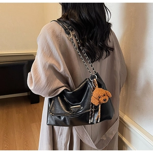 Detail of black hobo shoulder bag with metal chain strap and cute teddy bear charm