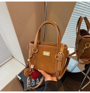 Detail of a brown suede bucket bag with gold logo, bead charms, and a versatile shoulder strap