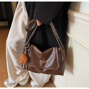 Detail of dark brown leather shoulder bag with gold metal chain and cute bear charm