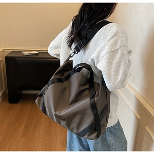 Dunkelgraue Reisetasche aus Nylon mit Umhängeriemen in wohnlicher Atmosphäre gezeigt