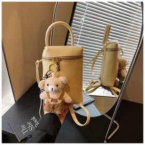 Vue détaillée d'un sac à main beige minimaliste avec un ourson en peluche sous une lumière douce