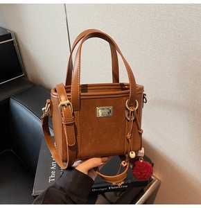 Detail of brown faux suede bucket bag featuring a gold nameplate and plush pendant