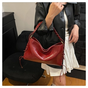 Détail d'un sac bandoulière en cuir rouge foncé avec lacets latéraux, franges et anse tressée