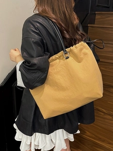 Large mustard yellow tote bag with black leather straps shown on a casual model