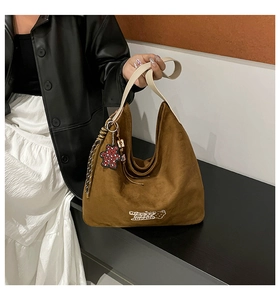 Detail of coffee brown suede hobo bag with white embroidery and bear pendant on shoulder