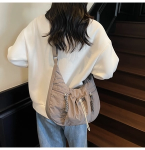 Close-up of grey ruched crescent bag with drawstring details and adjustable strap on a model