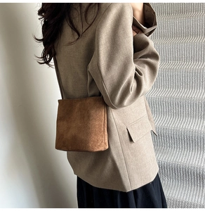 Detail of dark brown suede crossbody bag styled with a khaki blazer and black skirt