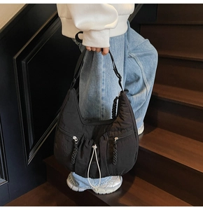 Detailed close-up of a black nylon crossbody bag with pleated texture and dual zippers