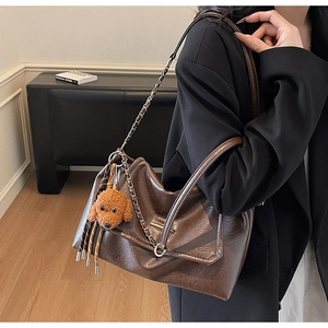 Detail of dark brown crinkled leather shoulder bag with a cute teddy bear plush charm