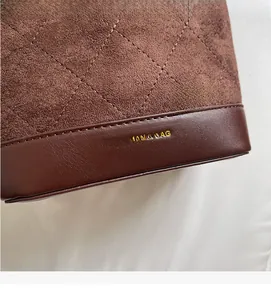Detail of dark brown suede bucket bag with diamond stitching and gold foil brand logo