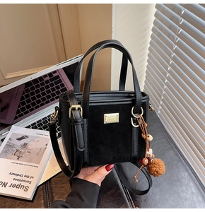 Detail of black suede and leather bucket bag with gold hardware and plush charm