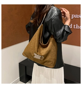 Brown suede bucket bag with bear embroidery worn by model against a neutral wall
