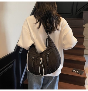 Model showing large black nylon crescent crossbody bag with pleated details and zip pocket