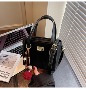 Detail of black suede shoulder bag with gold hardware and plush red pompom charm detail