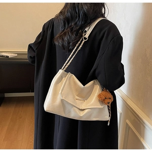 Detail of cream leather shoulder bag with gold metal trim and brown plush bear charm