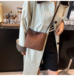 Détail d'un sac bandoulière en daim marron foncé porté par un mannequin en intérieur