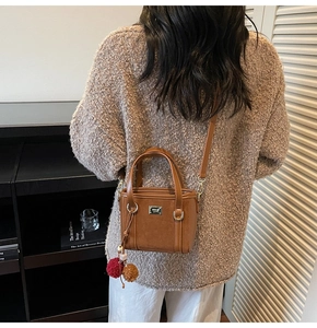 Rear view of model wearing a brown suede bucket bag with a plush pom-pom charm