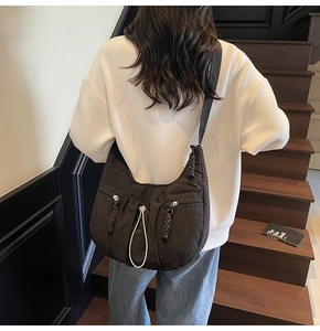 Detail of black nylon pleated crescent crossbody bag with woven zipper pulls and side pockets