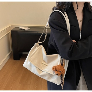 Detail of cream leather shoulder bag with gold chain and plush dog charm on black outfit