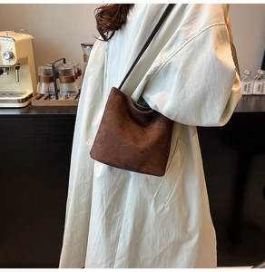Detail of dark brown matte suede bucket bag on a white coat in a cafe setting