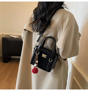 Detail of black suede bucket bag with gold logo plate and red pompom charm