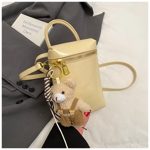 Détail d'un sac cylindrique beige avec un charm d'ours en peluche et finitions dorées