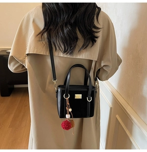 Detail of black crossbody bag with red-brown pompom charm and gold metal plate