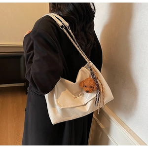 Detail view of cream leather shoulder bag featuring woven chain strap and teddy charm