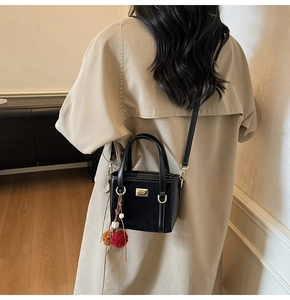 Black suede bucket bag with gold metal plate and plush charm on beige trench coat
