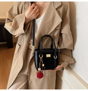 Detail of black suede shoulder bag with golden hardware and creative plush ball charm