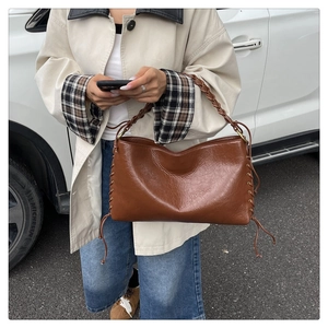 Détail du sac vintage en cuir marron avec bandoulière tressée et laçage sur les côtés