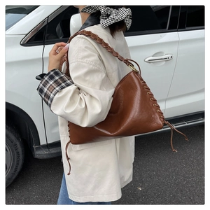Détail du sac vintage en cuir marron avec bandoulière tressée et œillets métalliques lacés