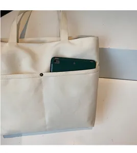 Close-up of durable cream canvas tote bag with functional front pocket and green device