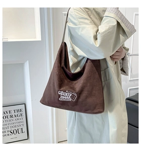 Close-up of brown suede tote bag featuring white linear embroidery and a wide shoulder strap
