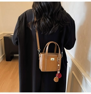 Detail of caramel tote bag with plush charms and logo plaque on a black wool coat