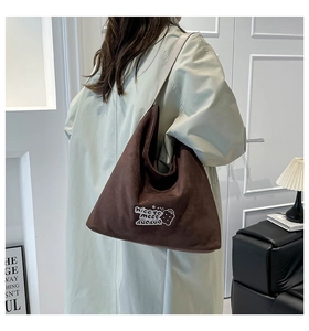 Detailed view of coffee brown corduroy shoulder bag with white embroidery on a model