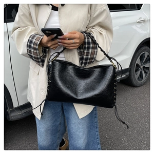 Détail du sac à bandoulière noir avec anse tressée et décoration de laçage latéral chic