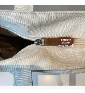 Detail of smooth silver zipper and brown leather puller on the beige canvas tote bag