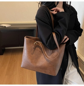 Detail of a brown oil-waxed PU leather tote bag with subtle fashion text embossing