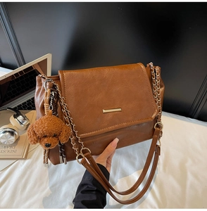 Detail of a brown leather vintage shoulder bag with gold chain and plush poodle charm