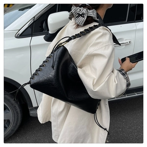 Détail du sac à épaule en cuir noir avec bandoulière tressée et œillets métalliques