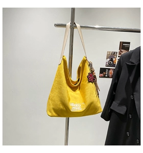 Close-up of yellow large tote bag with bear print and red floral charm on metal rack