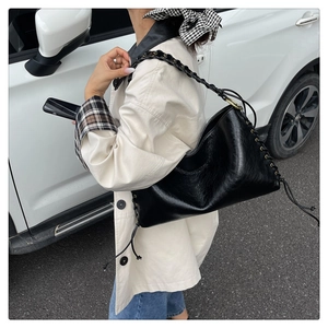Détail du sac croissant noir brillant avec bandoulière tissée et œillets métalliques
