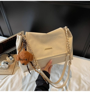 Detail of cream leather shoulder bag with gold chain strap and teddy dog charm