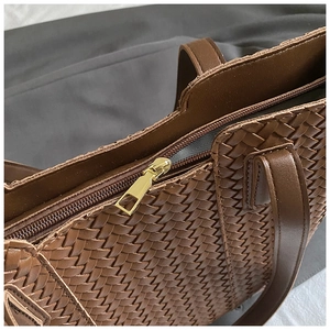 Close-up of the woven leather texture and golden zipper detail on a brown tote bag